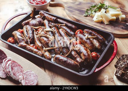 Grillpfanne mit leckeren hausgemachten Hühnchen-, Rind- und Schweinefleisch-Würstchen, Pilzen und Tomaten auf einem Holztisch mit Ketchup, Brot und Käse. Hoch Stockfoto