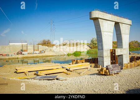 Große, moderne, graue Betonsäule im Fundament, umgeben von Metallpfählen. Dielen, Balken auf dem Boden, Holzprofile für den Bau von Brückenformen, Re Stockfoto