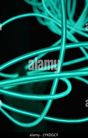 Chaotische Neonlinien sind spiralförmig angeordnet, Kreise, Drehungen mit der Hand einer Frau befinden sich auf schwarzem Hintergrund. Stockfoto
