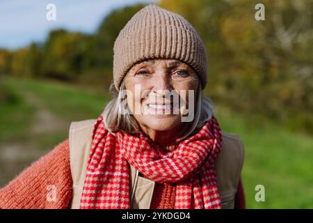 Porträt einer schönen älteren Frau mit grauem Haar. Weibliche Seniorin steht draußen in der Natur, blickt in die Kamera und lächelt. Stockfoto
