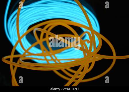 Hell leuchtende Elektrolumineszenzdrähte, gelb, orange, blau, himmelblau, türkisfarbene, dicke helle Linien. Chaotische Neonlinien sind spiralförmig angeordnet. Stockfoto