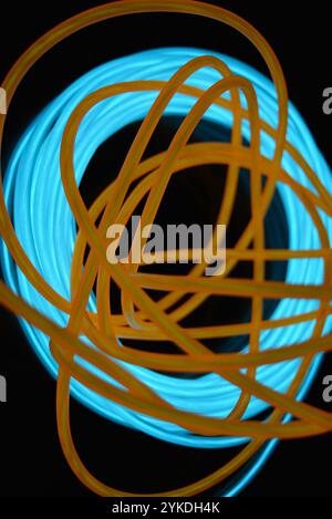 Hell leuchtende Elektrolumineszenzdrähte, gelb, orange, blau, himmelblau, türkisfarbene, dicke helle Linien. Chaotische Neonlinien sind spiralförmig angeordnet. Stockfoto