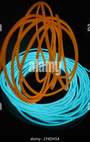Hell leuchtende Elektrolumineszenzdrähte, gelb, orange, blau, himmelblau, türkisfarbene, dicke helle Linien. Chaotische Neonlinien sind spiralförmig angeordnet. Stockfoto