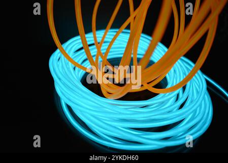 Hell leuchtende Elektrolumineszenzdrähte, gelb, orange, blau, himmelblau, türkisfarbene, dicke helle Linien. Chaotische Neonlinien sind spiralförmig angeordnet. Stockfoto