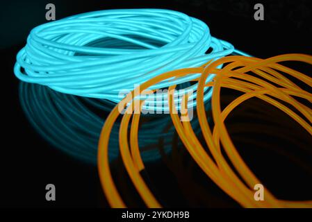 Hell leuchtende Elektrolumineszenzdrähte, gelb, orange, blau, himmelblau, türkisfarbene, dicke helle Linien. Chaotische Neonlinien sind spiralförmig angeordnet. Stockfoto