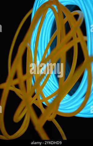 Hell leuchtende Elektrolumineszenzdrähte, gelb, orange, blau, himmelblau, türkisfarbene, dicke helle Linien. Chaotische Neonlinien sind spiralförmig angeordnet. Stockfoto