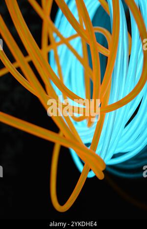 Hell leuchtende Elektrolumineszenzdrähte, gelb, orange, blau, himmelblau, türkisfarbene, dicke helle Linien. Chaotische Neonlinien sind spiralförmig angeordnet. Stockfoto