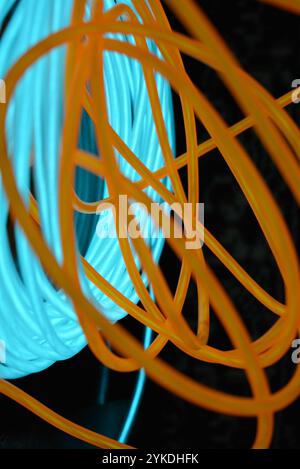 Hell leuchtende Elektrolumineszenzdrähte, gelb, orange, blau, himmelblau, türkisfarbene, dicke helle Linien. Chaotische Neonlinien sind spiralförmig angeordnet. Stockfoto