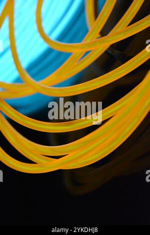 Hell leuchtende Elektrolumineszenzdrähte, gelb, orange, blau, himmelblau, türkisfarbene, dicke helle Linien. Chaotische Neonlinien sind spiralförmig angeordnet. Stockfoto