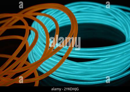 Hell leuchtende Elektrolumineszenzdrähte, gelb, orange, blau, himmelblau, türkisfarbene, dicke helle Linien. Chaotische Neonlinien sind spiralförmig angeordnet. Stockfoto