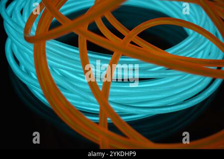 Hell leuchtende Elektrolumineszenzdrähte, gelb, orange, blau, himmelblau, türkisfarbene, dicke helle Linien. Chaotische Neonlinien sind spiralförmig angeordnet. Stockfoto