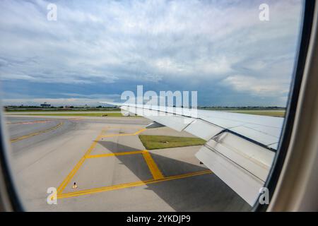 Durch das Flugzeugfenster wird der internationale Flughafen Suvarnabhumi, zusammen mit den weitläufigen Flügeln des Flugzeugs, in der Mittagsruhe sichtbar Stockfoto