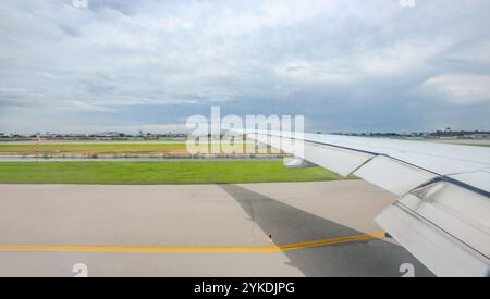 Durch das Flugzeugfenster wird der internationale Flughafen Suvarnabhumi, zusammen mit den weitläufigen Flügeln des Flugzeugs, in der Mittagsruhe sichtbar Stockfoto