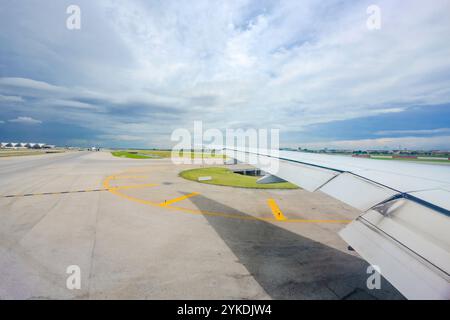 Durch das Flugzeugfenster wird der internationale Flughafen Suvarnabhumi, zusammen mit den weitläufigen Flügeln des Flugzeugs, in der Mittagsruhe sichtbar Stockfoto