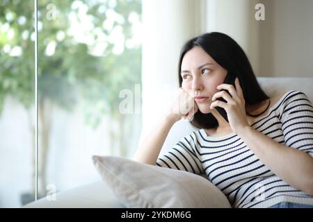 Gelangweilte asiatische Frau, die in einem Telefongespräch wartet und zu Hause auf einer Couch sitzt Stockfoto