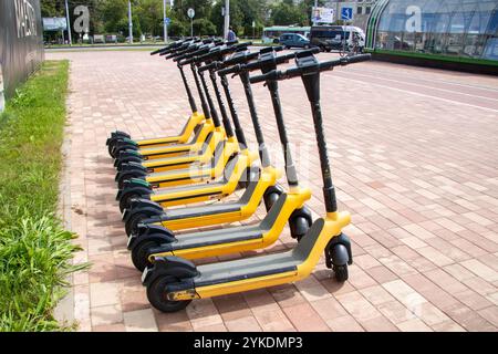 Weißrussland, Minsk - 18. juli 2024: Eine Reihe leuchtender gelber und eleganter schwarzer Roller parkt ordentlich auf einem geräumigen Parkplatz, der moderne urbane Farben zeigt Stockfoto