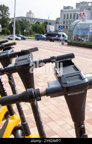 Weißrussland, Minsk - 18. juli 2024: Eine Reihe leuchtender gelber und eleganter schwarzer Roller parkt ordentlich auf einem geräumigen Parkplatz, der moderne urbane Farben zeigt Stockfoto