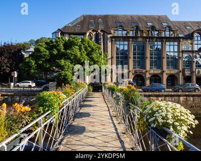 Quimper, Frankreich - 28. Juli 2024: Eine malerische Brücke mit bunten Blumen führt zu einem modernen Bürogebäude mit großen Fenstern. Stockfoto