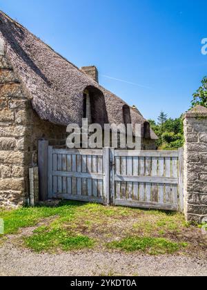 Ein rustikales Steinhaus mit einem Strohdach und einem Holztor in Kercanic, Bretagne, inmitten einer ländlichen Landschaft unter einem klaren blauen Himmel. Stockfoto