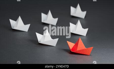 Leaderboat of Red Paper Ship Concept zwischen White Paper Ship. Key man und Business erfolgreich mit einer Richtung zusammen. Abbildung mit schwarzer Textur Stockfoto