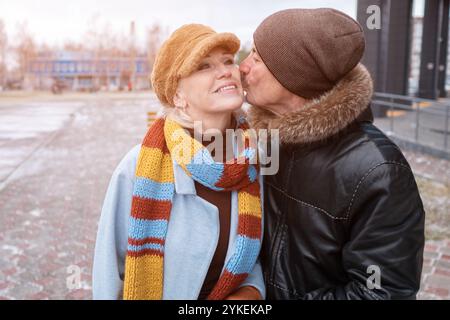 Älterer Mann, der Frau auf die Wange küsst, während er in der Winterstadt spaziert Stockfoto