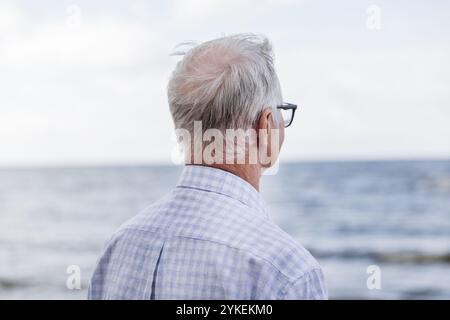 Ein älterer Mann steht am Strand und blickt auf die Skyline Stockfoto