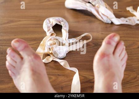 Nahaufnahme von Satin spitzenschuhen in der Nähe von unscharfen, müden Füßen einer Balletttänzerin Stockfoto