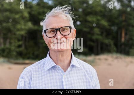 Porträt fröhlicher älterer Mann, der allein am Strand spaziert Stockfoto