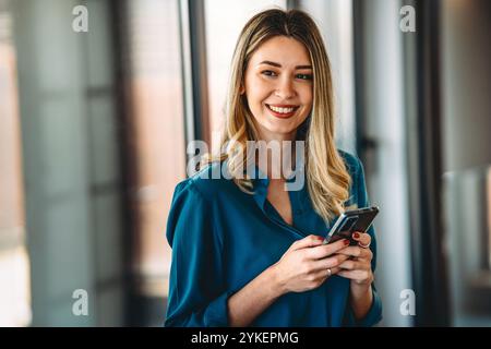 Junge glückliche, elegante, geschäftige Geschäftsfrau, Manager, die im Büro das Handy benutzt. Erfolg Stockfoto