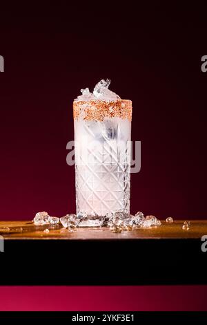 Ein Paloma-Cocktail in einem gemusterten Glas, verziert mit einem gesalzenen Rand und gefüllt mit erfrischendem Eis. Das Getränk steht vor einer stimmungsvollen, dunklen Kulisse Stockfoto