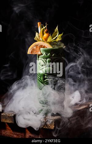 Ein lebendiger Tiki-Cocktail, garniert mit frischen Zitrusfrüchten und tropischen Früchten, serviert in einem aufwendig gestalteten grünen Keramikbecher Stockfoto