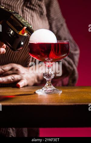 Ein vibrierender Negroni-Cocktail in einem Kristall-Coupé-Glas mit einer fesselnden Rauchblase auf der Oberseite dieser ikonische italienische Aperitif kombiniert Gin, Stockfoto