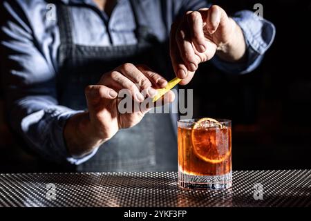 Ein Barkeeper garniert gekonnt einen klassischen Whiskey altmodischen Cocktail mit einem Hauch von Zitruspeel the Drink, serviert in einem Steinglas, strahlt sop aus Stockfoto