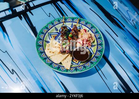 Farbenfrohe Teller mit Hühnerherzen Yakitori Spießen mit gemischtem Salat, serviert auf einem gemusterten Teller über einem leuchtend blauen Tisch in einem Restaurant in Stockfoto