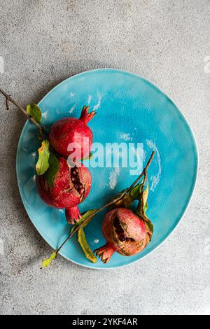 Draufsicht auf drei reife Granatäpfel, einer aufgespalten, auf einer leuchtend blau strukturierten Platte, vor grauem Hintergrund. Stockfoto