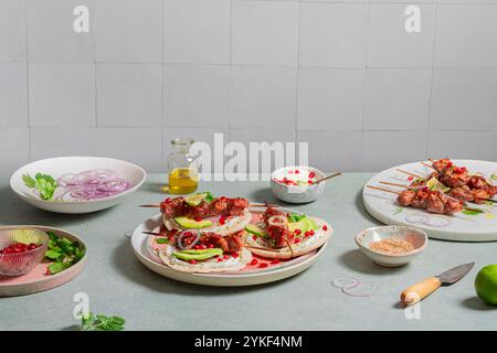 Arrangiertes Festmahl mit Spießen mit Joghurtsauce, Granatapfelkernen und Avocadoscheiben auf Naan-Brot. Die Kulisse zeigt verschiedene Gerichte inklusive Stockfoto