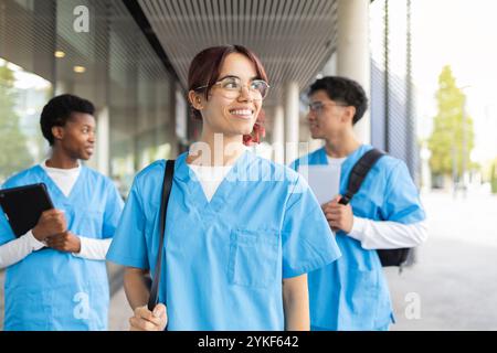 Eine fröhliche Gruppe multirassischer Pflegestudenten, die auf einem Universitätscampus lässig spazieren gehen und plaudern Stockfoto