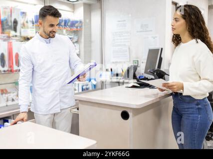 Eine freundliche Interaktion in einem Orthopädie-Laden Ein Mitarbeiter in einem weißen Mantel hilft einem Kunden, Regale mit medizinischem Zubehör sind sichtbar Stockfoto