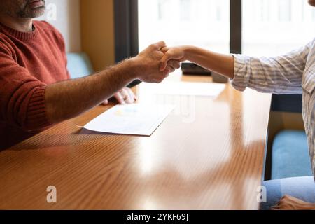 Eine Nahaufnahme eines Handschlags über einem Holztisch in einem modernen Coworking-Raum, symbolisiert Zusammenarbeit und Partnerschaft, Eine zwanglose und kreative Umgebung Stockfoto