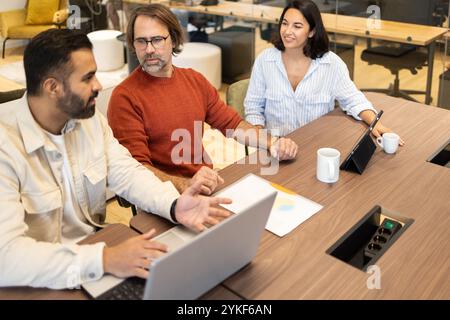 Eine Gruppe von verschiedenen Fachleuten, die sich in einem modernen Coworking-Raum unterhalten. Die Atmosphäre ist ungezwungenermaßen, mit warmer Beleuchtung und modernem Ambiente Stockfoto