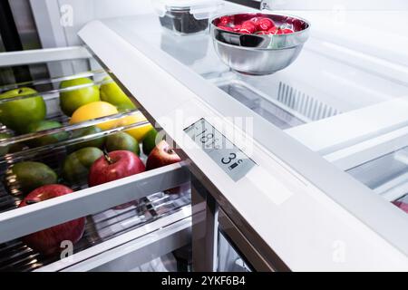 Der moderne Küchenkühlschrank ist geöffnet und bietet eine Auswahl an frischem Obst, einschließlich grüner Äpfel, roter Äpfel und Zitronen, sowie eine klare Temperatur Stockfoto
