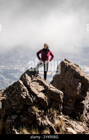 Ein Wanderer steht selbstbewusst auf einem felsigen Gipfel und blickt in die Ferne. Die bewölkte Kulisse verleiht der atemberaubenden Aussicht auf die Berge eine dramatische Note Stockfoto