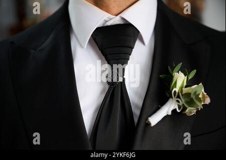 Zugeschnittene, nicht erkennbare Nahansicht der formellen Kleidung eines männlichen Bräutigams mit einer detaillierten schwarzen Krawatte und einer weißen rosa Boutonniere. Stockfoto