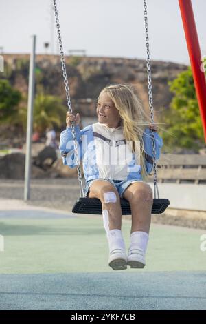 Eine fröhliche junge Frau mit Stuve-Wiedemann-Syndrom, die medizinische Flecken und Narben trägt, genießt ihre Zeit auf einer Spielplatzschaukel und zeigt ihre Widerstandsfähigkeit Stockfoto