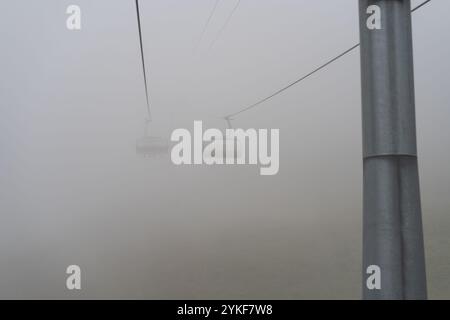Geheimnisvoller Blick auf die Seilbahnen, die in dichtem Nebel verschwinden. Das Bild fängt die unheimliche Ruhe von Stoos in der Schweiz mit einem Fokus auf die Kabelübertragung ein Stockfoto