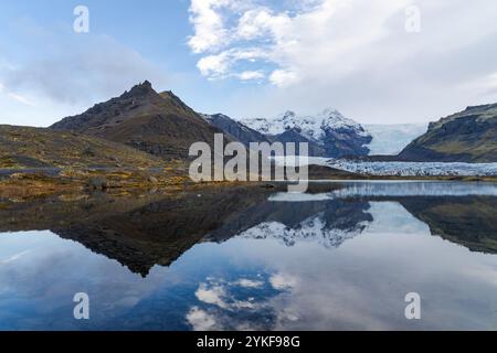 Eine ruhige isländische Landschaft zeigt einen glasklaren See, der einen scharfen Berggipfel reflektiert, vor dem Hintergrund von Gletschern und Herbstlaub. Stockfoto