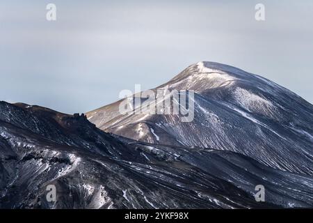 Ein atemberaubender Blick auf einen schneebedeckten Berggipfel im isländischen Hochland mit seinen schlanken, kurvengesäumten Hängen unter weichem Licht. Stockfoto