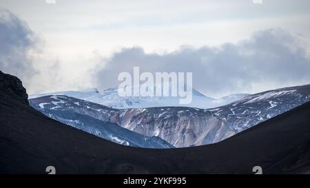 Eine ruhige Szene, die die ruhige Schönheit des isländischen Hochlands mit schneebedeckten Gipfeln unter einem weichen, bewölkten Himmel, umgeben von einem subtilen Ohr, einfängt Stockfoto
