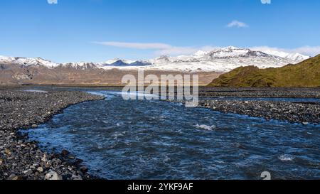 Der Fluss fließt durch die zerklüfteten Highlands Islands, vor dem Hintergrund schneebedeckter Berge, der leuchtend blaue Himmel und felsiges Gelände ergänzen die Landschaft Stockfoto