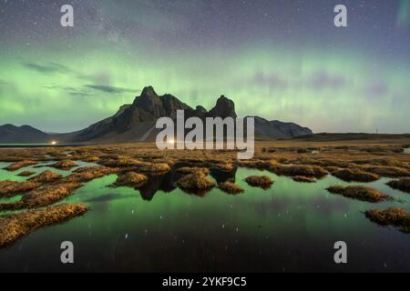 Ein atemberaubender Blick auf die Nordlichter, die die zerklüftete Landschaft von Eystrahorn, Krossanesfjall, Island, mit Reflexionen im ruhigen Wasser A beleuchten Stockfoto